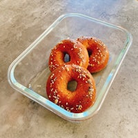 three bagels in a clear container with sesame seeds