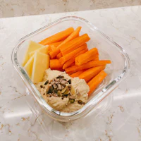 a glass bowl with carrots and hummus
