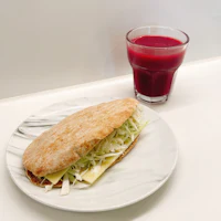 a sandwich on a plate next to a glass of juice