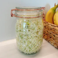 cabbage in a glass jar next to a basket of bananas