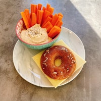 a plate with a bagel, carrots and hummus