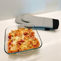 an oven mitt on a table next to a dish of pasta