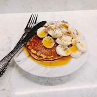 a plate of pancakes with banana slices and a fork