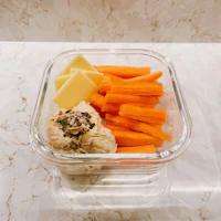 a glass container with carrots, cheese and hummus