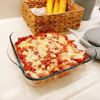 a dish of lasagna on a counter next to a basket of corn