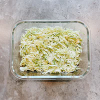 shredded cabbage in a glass bowl on a concrete floor